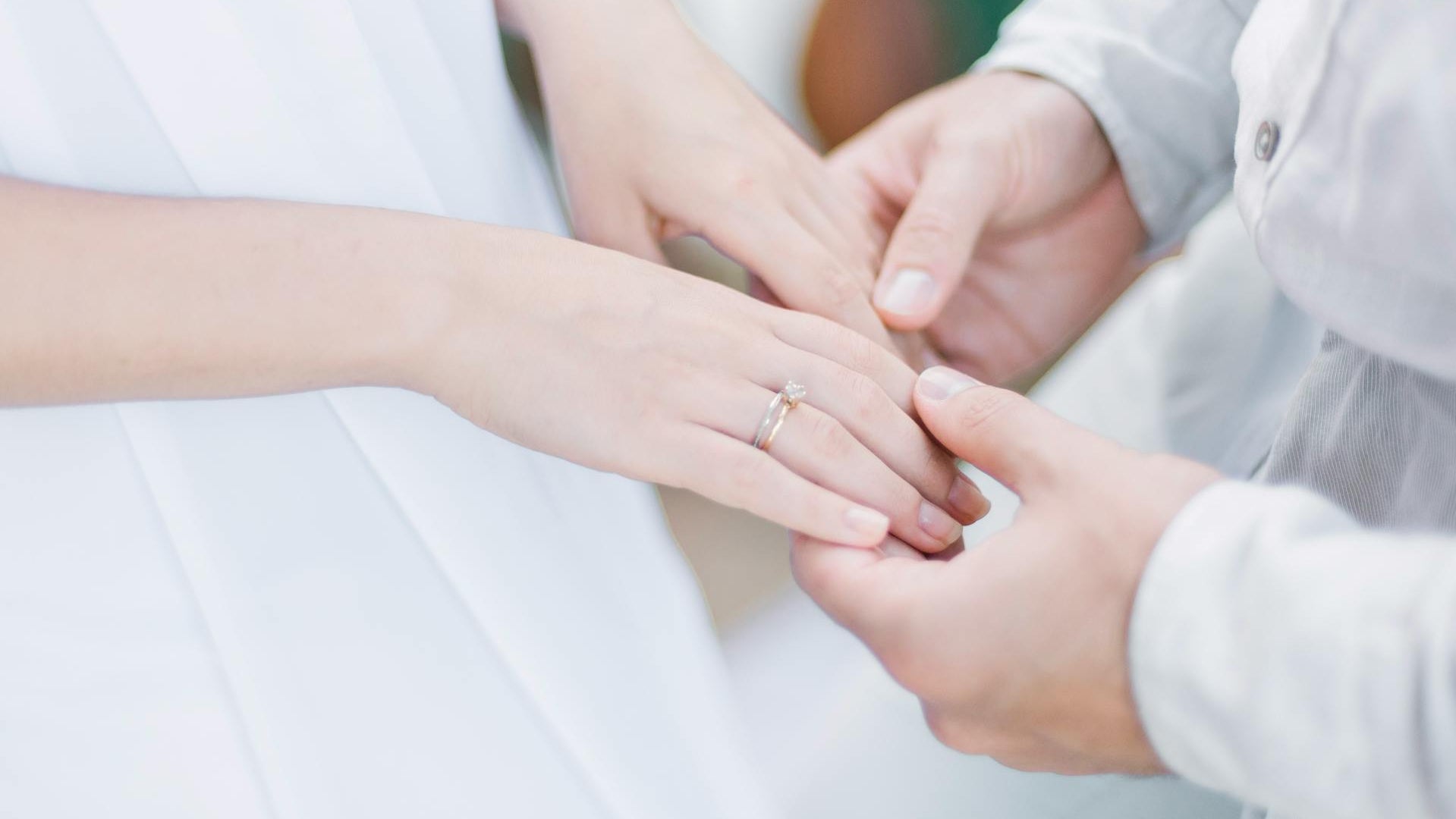 Close-up of two hands holding each other with a wedding ring on one finger.